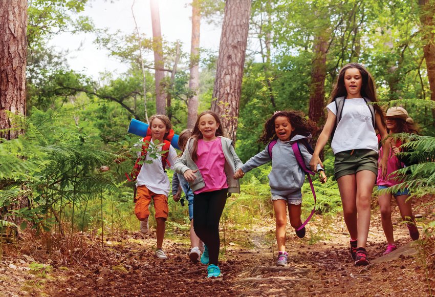 Boys and girls running in the forest together holding hands on a trail during a nature trip.