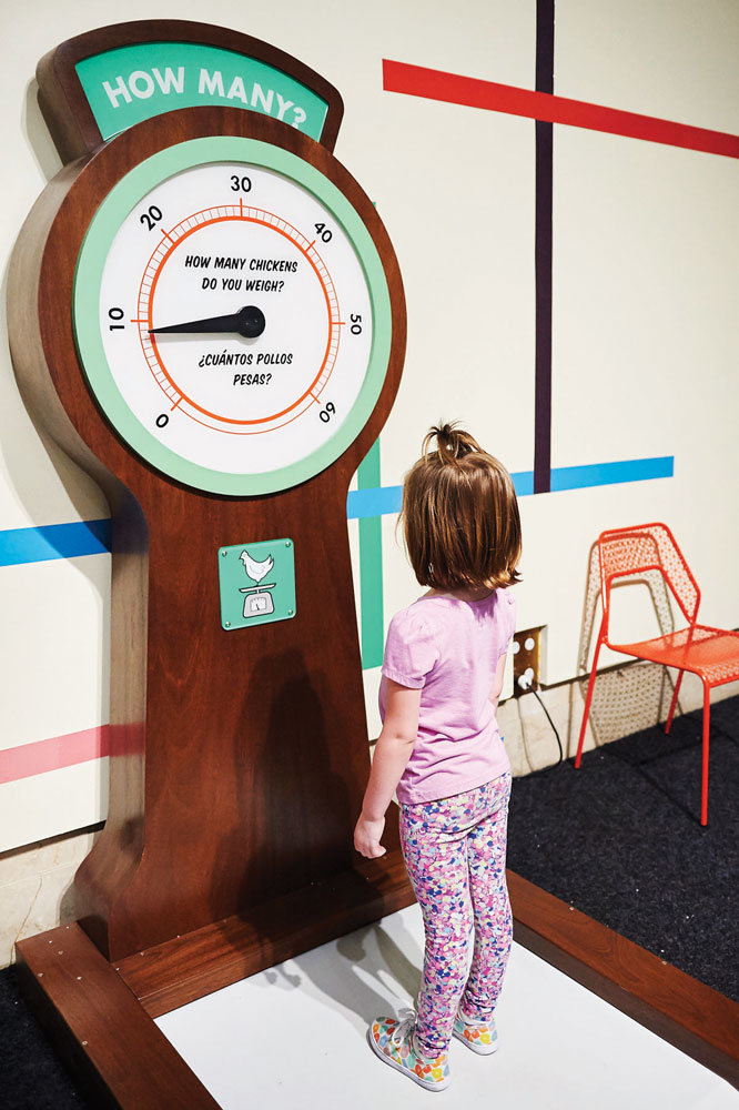 A child visiting the “Measurement Rules” exhibit learns how many chickens she weighs.