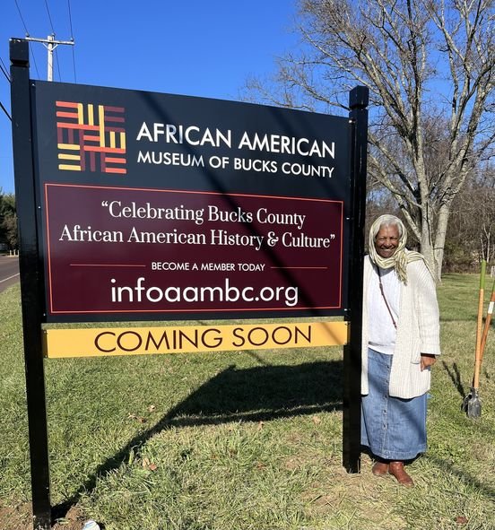 Linda Salley, president and executive director of the African American Museum of Bucks County, poses in front of the sign where the museum will be at the Boone Farm in Middletown Township.