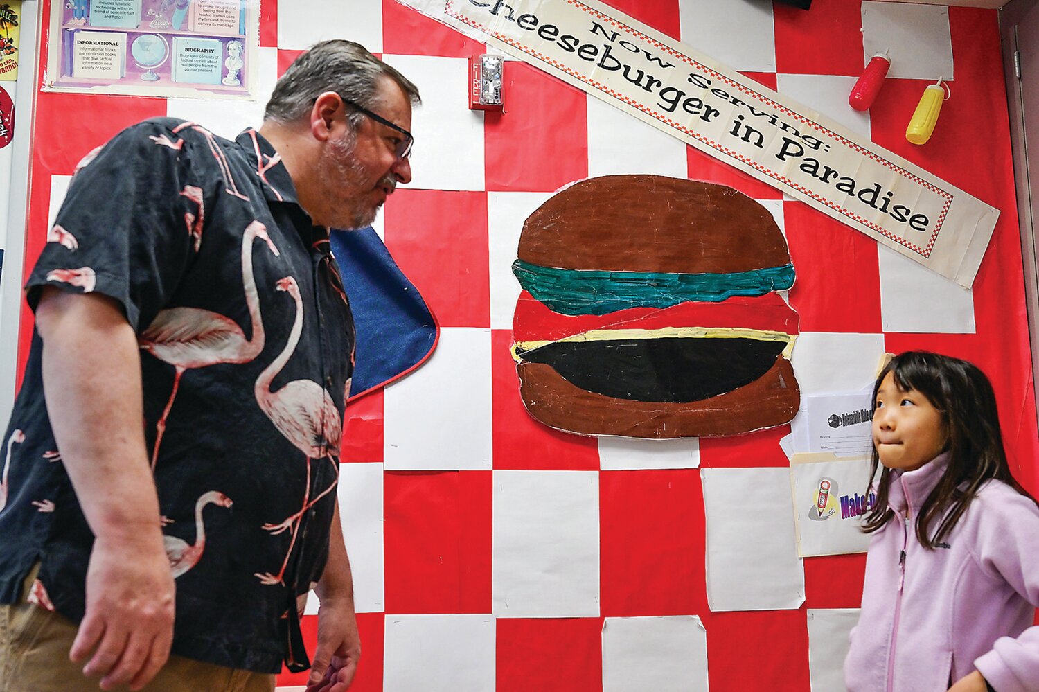 Jim Molenari stands next to a Jimmy Buffet-themed reading poster as student Claire Zhai glances at him. Molenari is known as a Jimmy Buffet superfan. His classroom is a place everyone calls Molenariville, likened to Margaritaville.