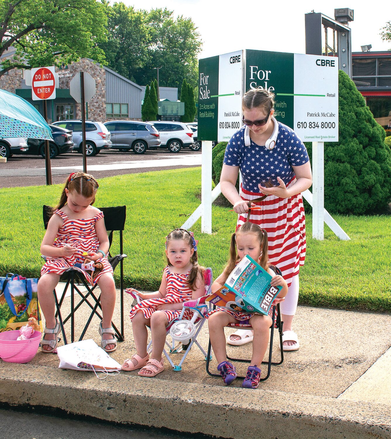 Mom Ashley Taylor does the hair of Penny Baker, right, as Reilly Baker, left, and Avi Taylor sit along the parade route.