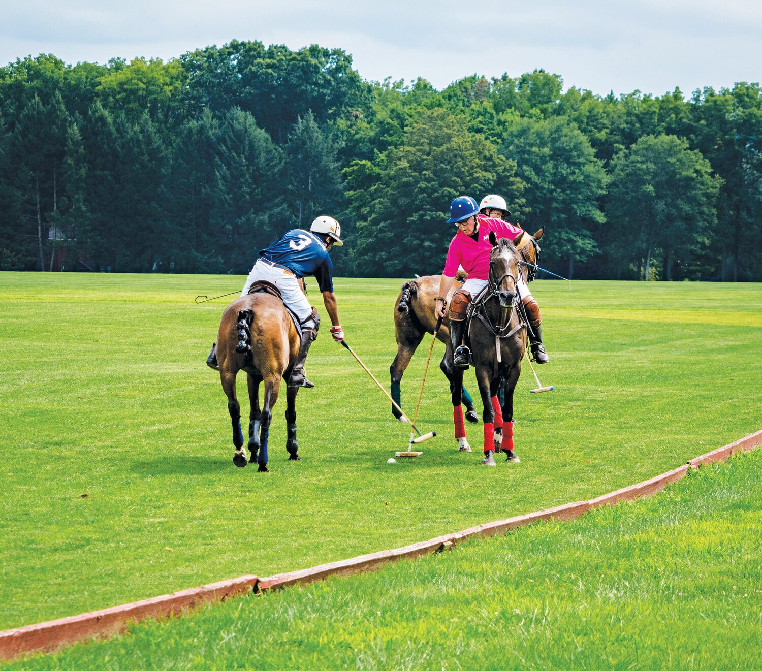 Polo players reach down with their mallets to hit the ball.