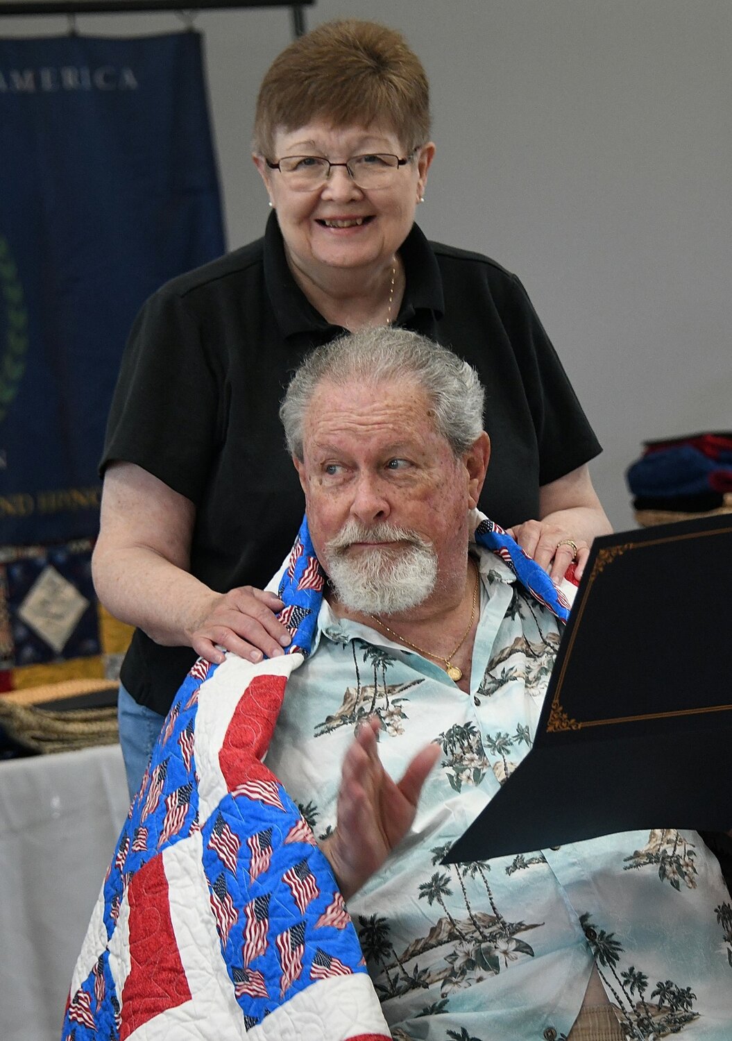 John Snyder, with his wife, is wrapped in a quilt given by the Quilts of Valor.