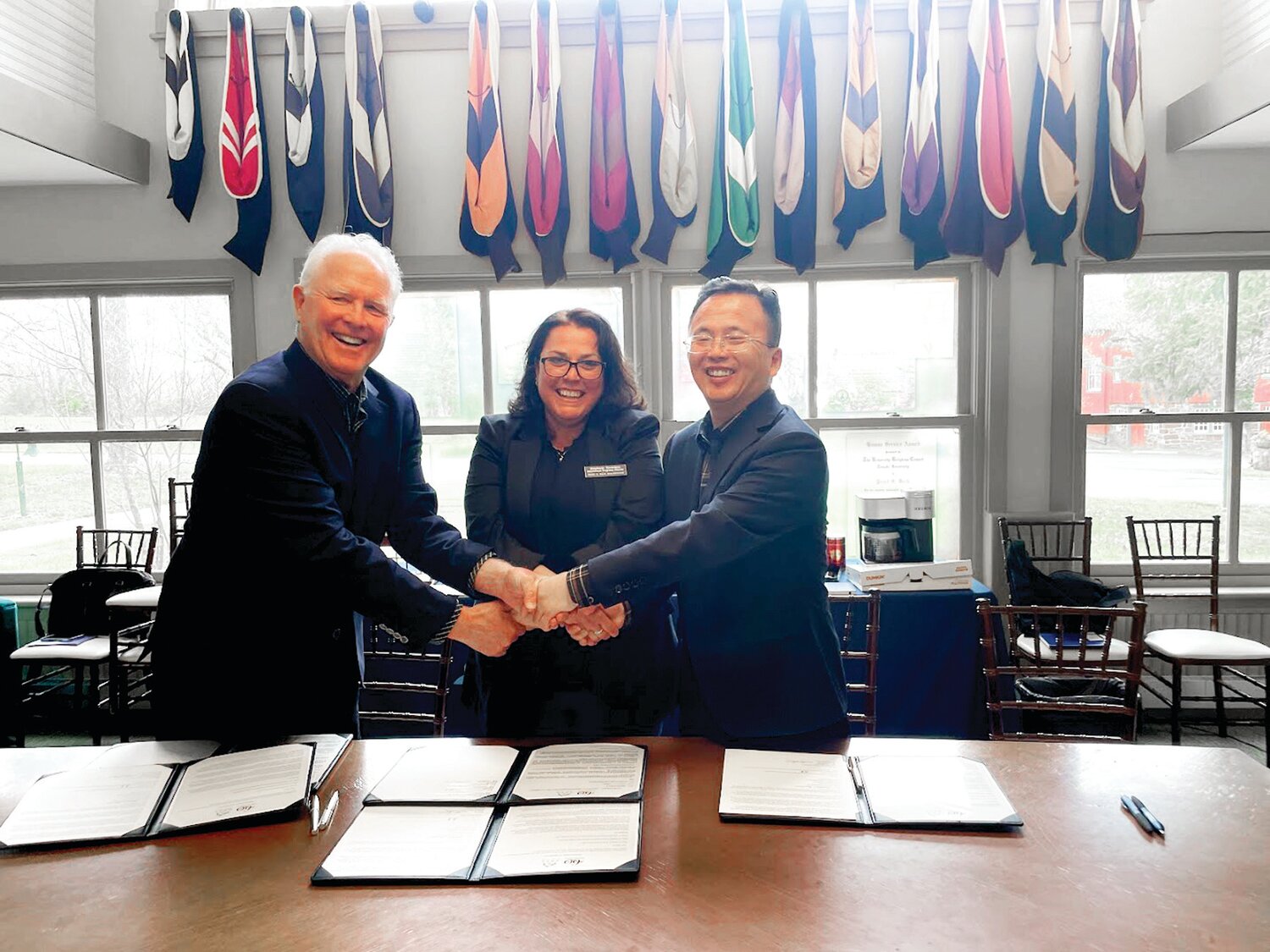 Steve Harnsberger, founder of PPX in San Francisco; Stephanie Saveriano, international programs director for Pearl S. Buck International; and Yuan Yong, deputy mayor of Lushan City, China, shake hands after signing a memorandum of agreement for a museum and cultural exchange program.