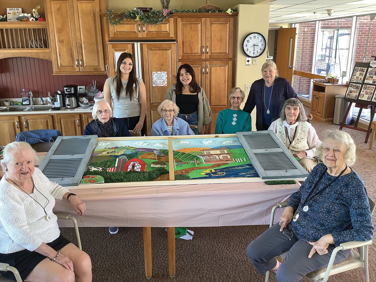 Temple University art therapy interns Jenna Rosenblatt and Julie Vasquez and Personal Care residents at The Willows of Living Branches, surround the 7-foot farmland mural created for residents living with dementia at Souderton Mennonite Homes.