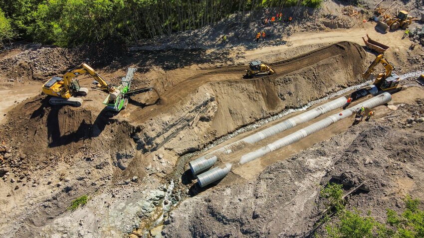 Crews are seen from above as pipes are placed and dirt is moved to create a traversable path along Spirit Lake Highway in Castle Rock following a landslide in May 2023.