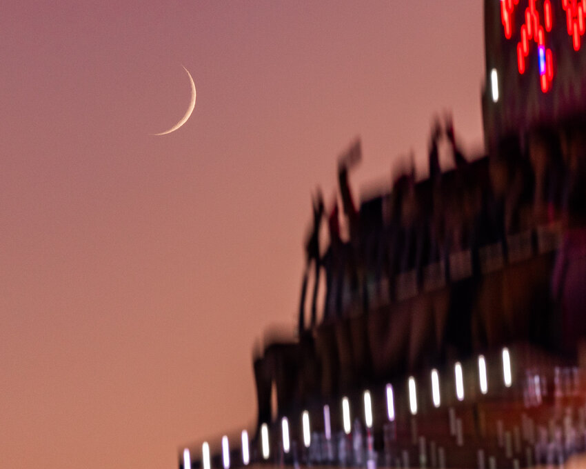 The moon is seen at sunset at fairgoers raise their hands on a ride at the Southwest Washington Fairgrounds on Friday, Aug. 19.