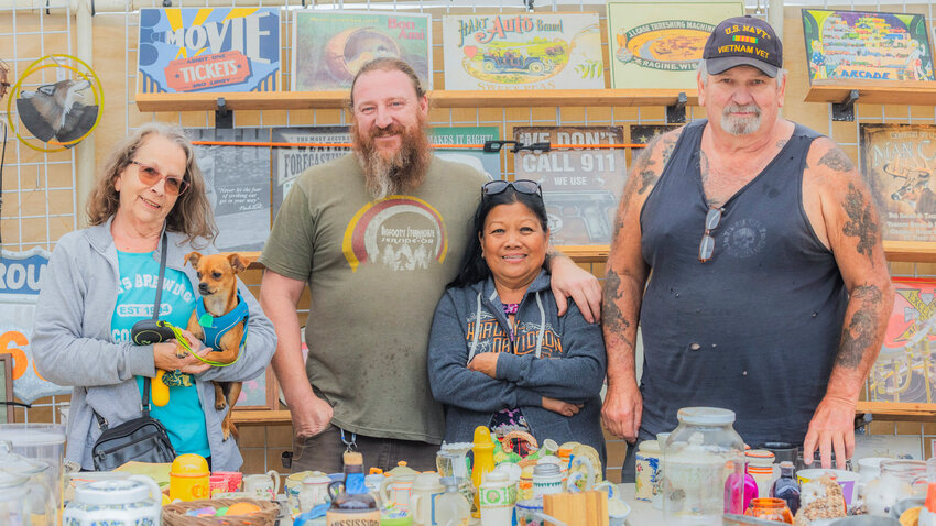 From left, Packwood flea market vendors Sue Black (with Chihuahua mix &ldquo;Charlie&rdquo;), Scott Christensen, and Romeo and Tony Tarnowski smile for a photo in their booth on Thursday.