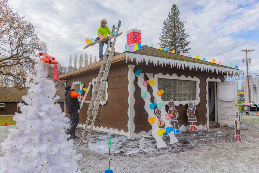Terry Harris organizes panels on the roof of a building at Henderson Park as a gingerbread house takes shape Saturday in Chehalis.