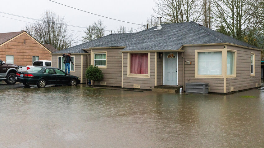 A man walks across the hood of a car to avoid ankle deep water around a residence along Southwest Snively Ave. in Chehalis on Tuesday, Dec. 5.