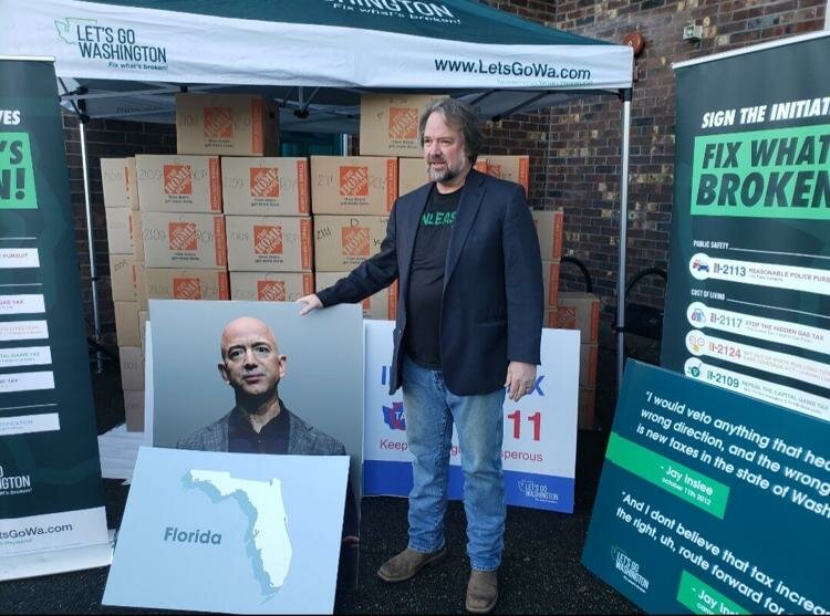 Let's Go Founder Brian Heywood poses in front of boxes of initiative signatures, along with a photo of billionaire Amazon founder Jeff Bezos and the state of Florida. Bezos announced earlier this year he intends to move from Washington to Florida.