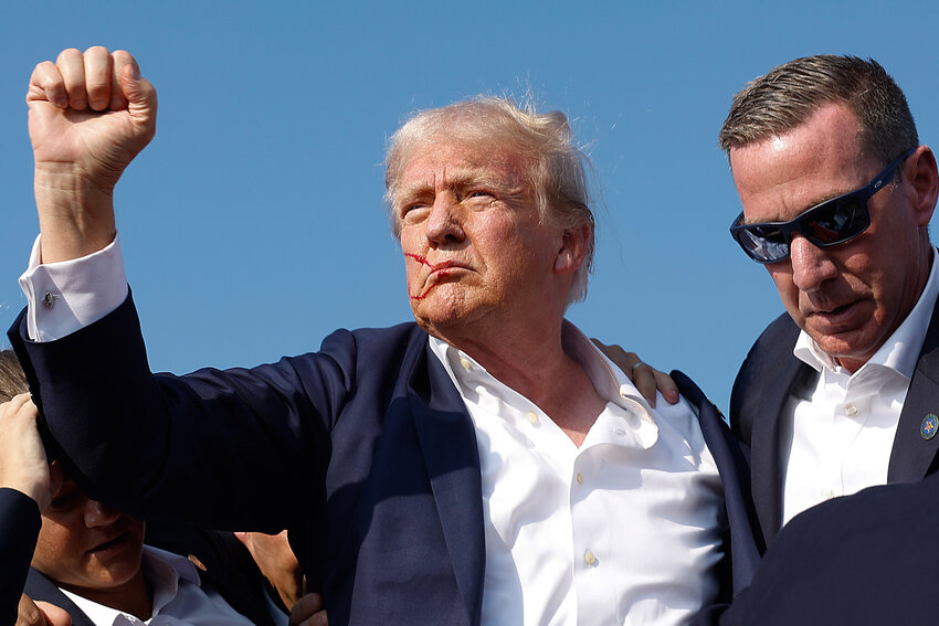 Republican presidential candidate former President Donald Trump pumps his fist as he is rushed offstage by U.S. Secret Service agents after being grazed by a bullet during a rally on July 13, 2024 in Butler, Pennsylvania. Butler County district attorney Richard Goldinger said the shooter is dead after grazing former U.S. President Donald Trump with a bullet, killing one audience member and injuring another in the shooting. (Photo by Anna Moneymaker/Getty Images)