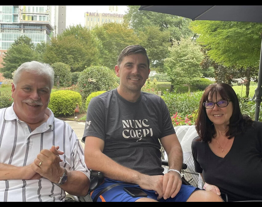 Brock Peterson (center) poses for a photo at his home in Virginia Beach, Virginia with his parents Cathy and Norm Peterson. Cathy moved from Washington to Virginia to be Brock&rsquo;s full-time caregiver when Brock became paralyzed.