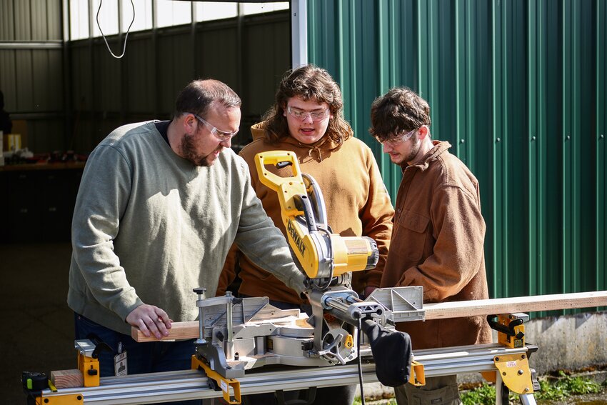 Jeffrey Burgess shows Tamaas Wakefield and Aaron Bell how to use the wood saw during construction class at Yelm High School on Oct. 10.