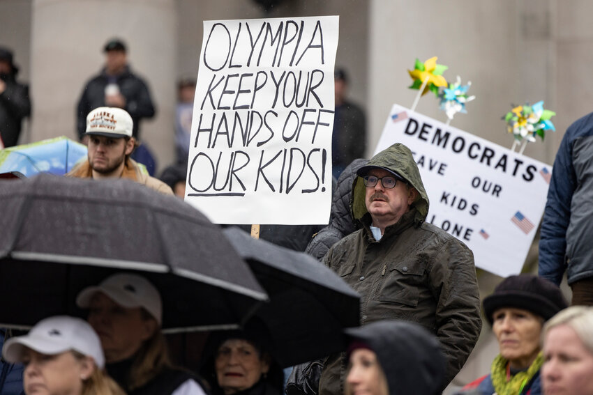A rally participant stands with a sign about parents’ rights during a rally on the steps of the Capitol in Olympia on Saturday, Feb. 15.