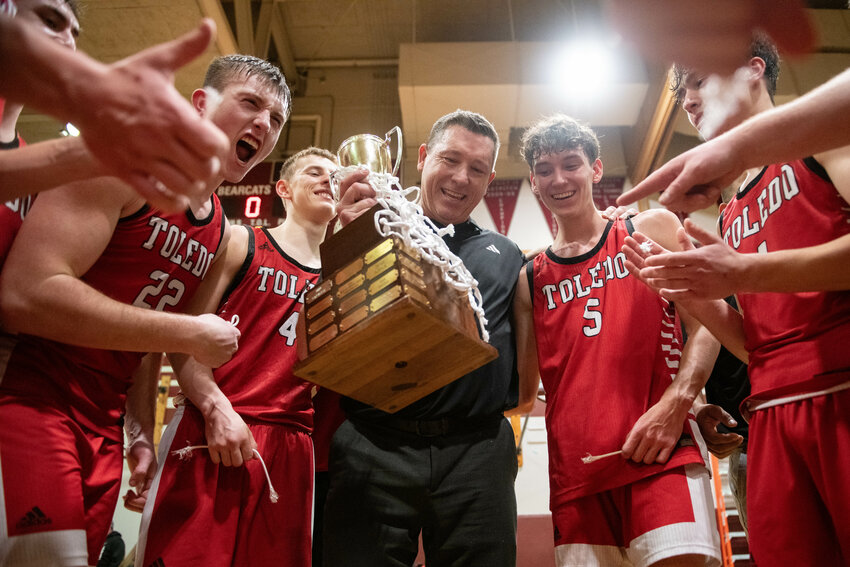 Toledo head coach Grady Fallon holds the 2B District 4 Championship Trophy while celebrating with his players after the Riverhawks&rsquo; 60-59 overtime win over Adna at W.F. West High School in Chehalis on Saturday, Feb. 22.