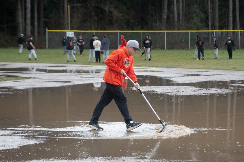 Rainier High School baseball head coach Justin Gurnsey pushes water from a flooded infield during a rainy practice on March 13.