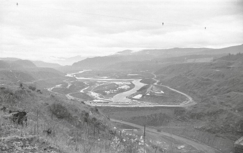"When Mossyrock Dam is completed in 1967, the ramified channels of the Cowlitz River east of the construction site will slowly rise, converging until the whole valley is covered. In the far foreground is what was Riffe, the community whose residents have moved away because of the Dam. The White Pass Highway, which now travels to the right of the river, will be rerouted through Morton. Work on the road is continuing as the dam is being built." — originally published The Daily Chronicle on Dec. 10, 1966
