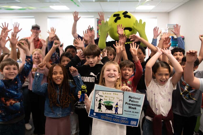 Jefferson Lincoln third grader Aubree Huber smiles while holding a trophy and poster featuring her winning artwork as classmates cheer during a classroom party honoring her for winning the Washington Poison Control Center&rsquo;s annual statewide poster contest in Centralia on Friday, May 9.