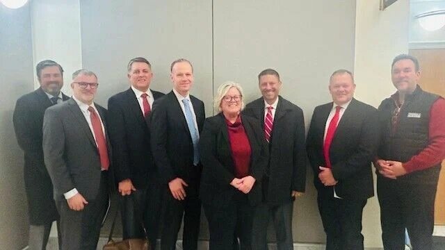 Trucking industry leaders pose for a photo at a Feb. 21, 2025 hearing for a bill to delink Washington from California trucking emissions standards. From right to left are Mike Chester, Peninsula Truck Lines; Sen. Matt Boehnke; Steve Gordon, Gordon Truck Centers; Sheri Call, Washington Truck Associations; Carl Hergart, Paccar Powertrain; Jeff DeVere, lobbyist for Washington Trucking Association; Mike Ennis, also a lobbyist with WTA; John Barnes, with Tec Equipment.