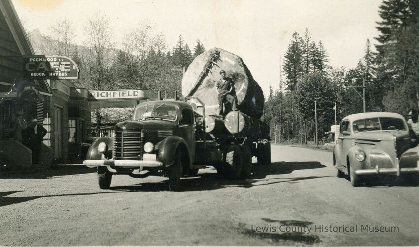 "An International log truck is loaded with a huge old growth log and two smaller logs in front of Brook Haynes Cafe and Tavern in Packwood in 1935 or 1936. A Studebaker car is parked in the road." (Lewis County Historical Museum)