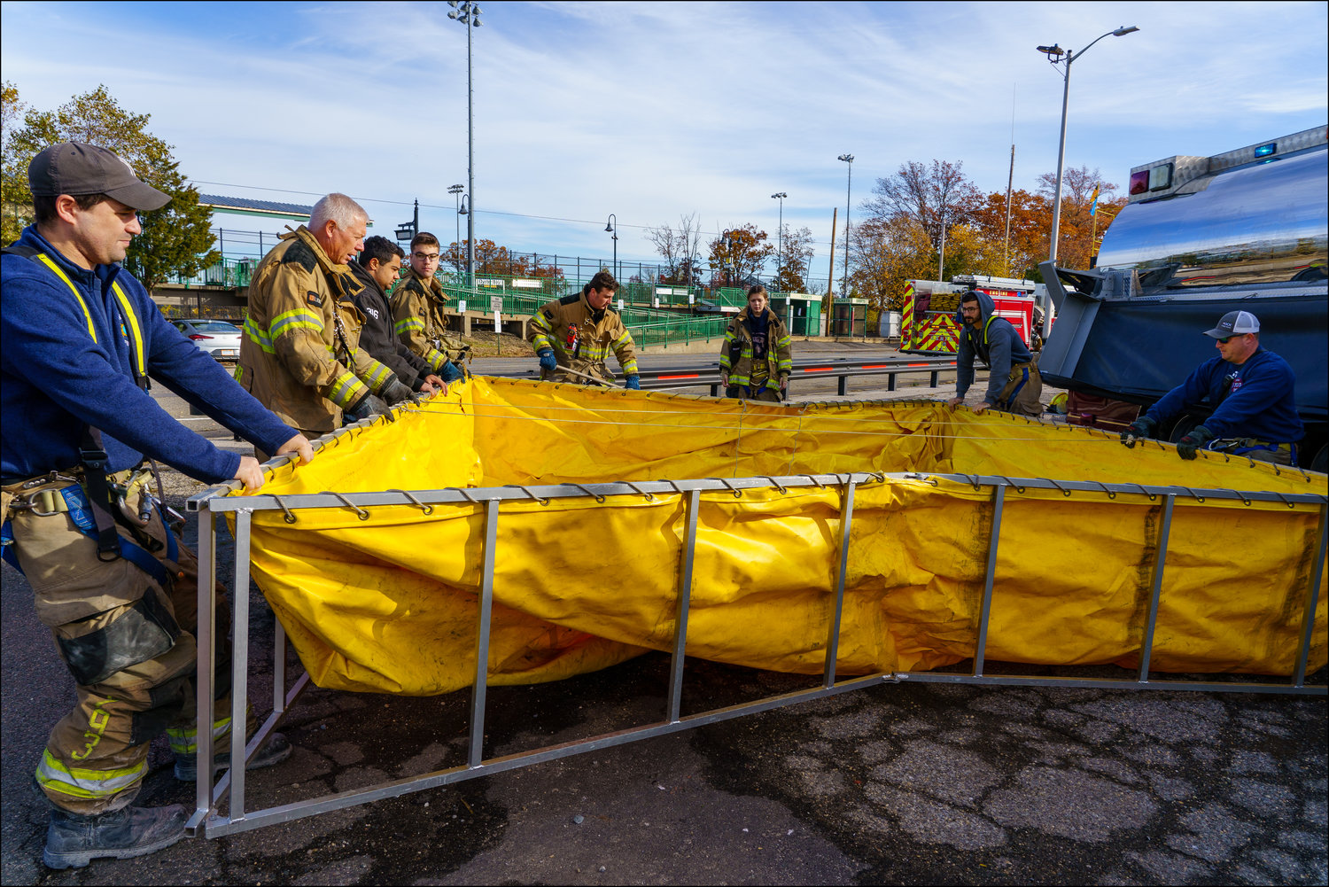 At a fire, a collapsible pool will be opened on level ground by firefighters in preparation for the water that will be dumped into it from a tanker truck.