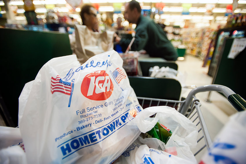 A cart full of plastic bags filled with groceries waits to be taken out to the parking lot at Bailey's IGA in Rochester as Floor Manager Nick Blanksma helps a customer with the credit card machine on Thursday afternoon.