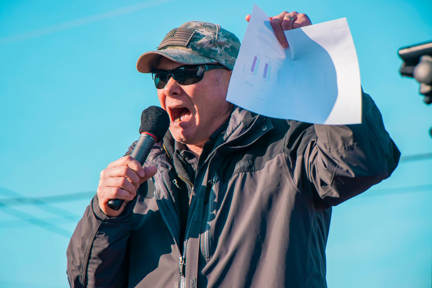 Robert J. Sutherland, a former member of the Washington State House of Representatives, holds up a piece of paper with charts showing total deaths in Washington state over the past five years while speaking during a freedom rally in downtown Mossyrock.