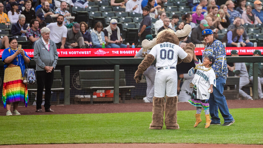 Payton KillEagle, a 7-year-old Mariners fan and cancer survivor, jumps up with her tongue out to high-five the Mariners Moose mascot after throwing out the first pitch as she is celebrated during Native American Heritage Night in Seattle on Monday, Aug. 28, 2023.