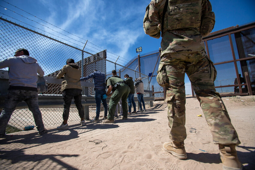 A Texas National Guardsman observes as Border Patrol agents pat down migrants who have surrendered themselves for processing, May 10, 2023. (Photo by Corrie Boudreaux for Source NM)