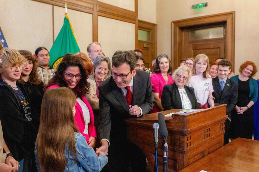Gov. Bob Ferguson hands over one of the pens he used to sign House Bill 1296, the &lsquo;students bill of rights&rsquo; to a child who attended the bill signing. (Photo by Jacquelyn Jimenez Romero/Washington State Standard)