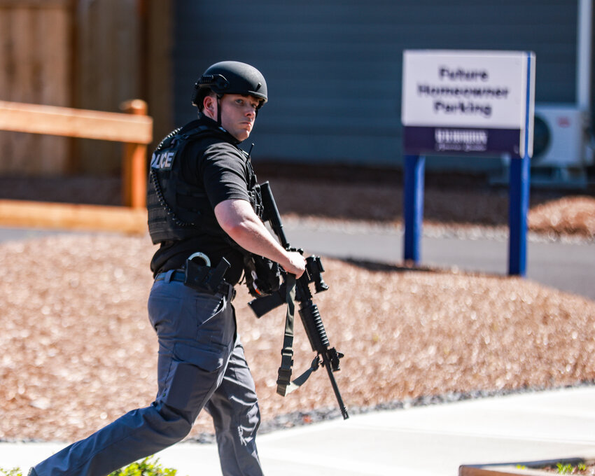 A Battle Ground police officer runs with an assault rifle to an active scene of a homicide with two deceased victims on arrival and one later transported by ambulance from a home at the 2100 block of Northeast Second Avenue in Battle Ground on Tuesday, June 3.