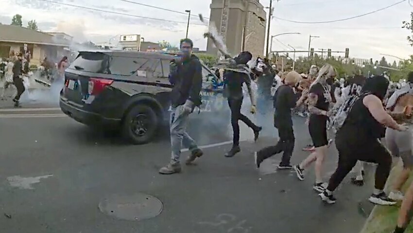 A protester throws a smoke canister back at Spokane police officers and sheriff deputies.