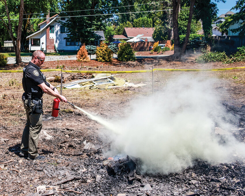 Clark County Sheriff&rsquo;s Office deputy Clint Fraser tries to subdue flames at the site of a Clark-Cowlitz Fire Rescue training burn where the fire started to pick up from hot spots in the rubble due to wind on Monday, June 30.