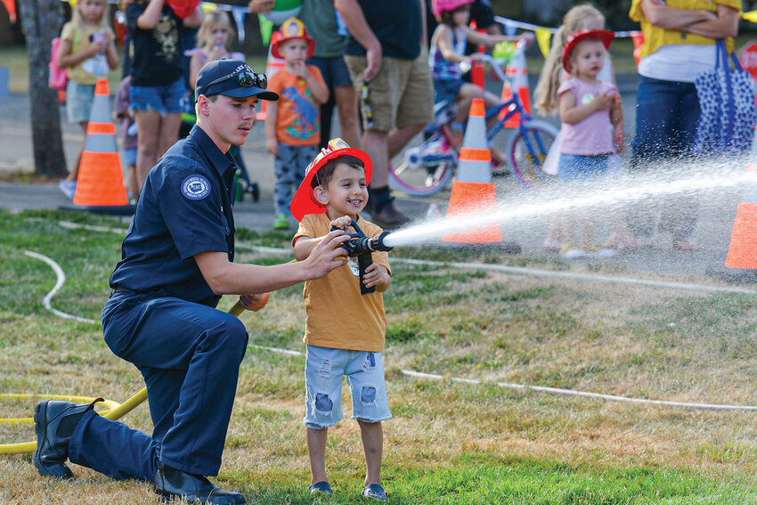 A Clark County Fire District 3 EMT guides youth to use the water hose during National Night Out on Aug. 5 at Kiwanis Park. The station&rsquo;s hose activity was one of several safety-themed events for youth.