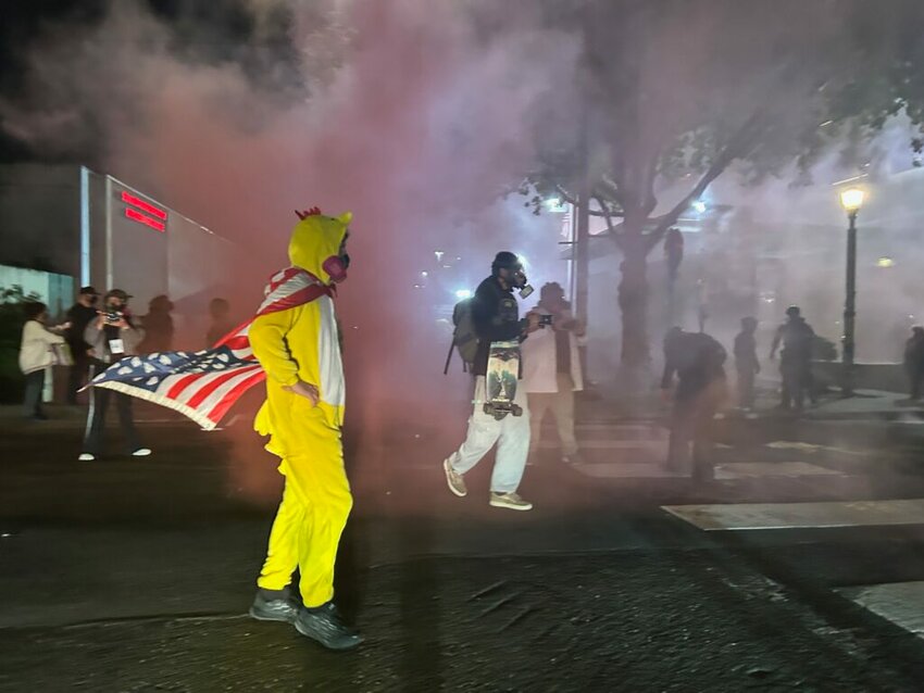 A protester dressed in a chicken suit against a backdrop of pink smoke deployed by federal agents at the Immigration and Customs Enforcement facility in Portland on Sunday, Oct. 5, 2025. (Photo by Alex Baumhardt/Oregon Capital Chronicle)