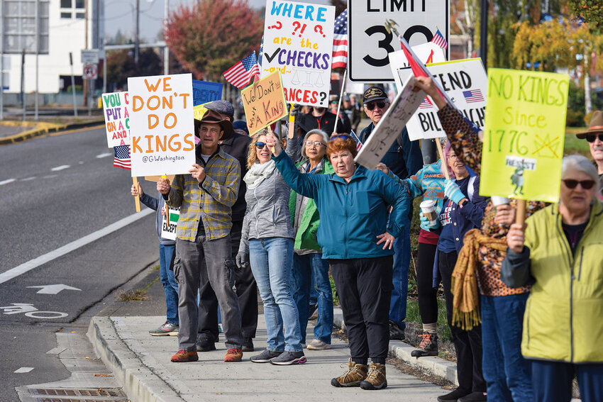 Protesters wave signs and flags on the northwest corner of the state Route 503 and state Route 502 intersection in Battle Ground on Saturday. The rally was part of the nationwide &ldquo;No Kings&rdquo; protest opposing what participants describe as authoritarian policies by President Donald Trump.