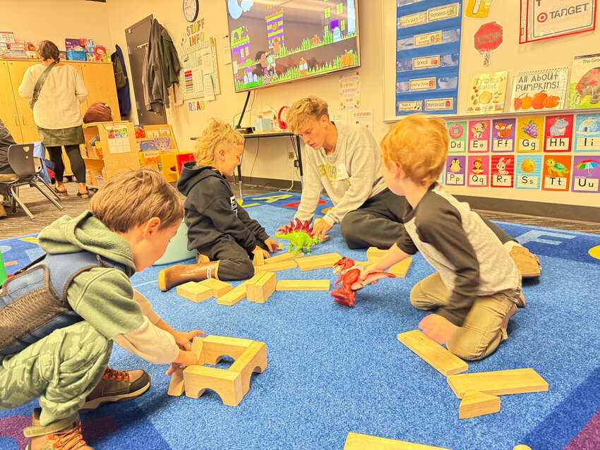 A Ridgefield High School student studying child development leads preschoolers at the Ridgefield Early Learning Center in an educational activity featuring colorful dinosaurs.