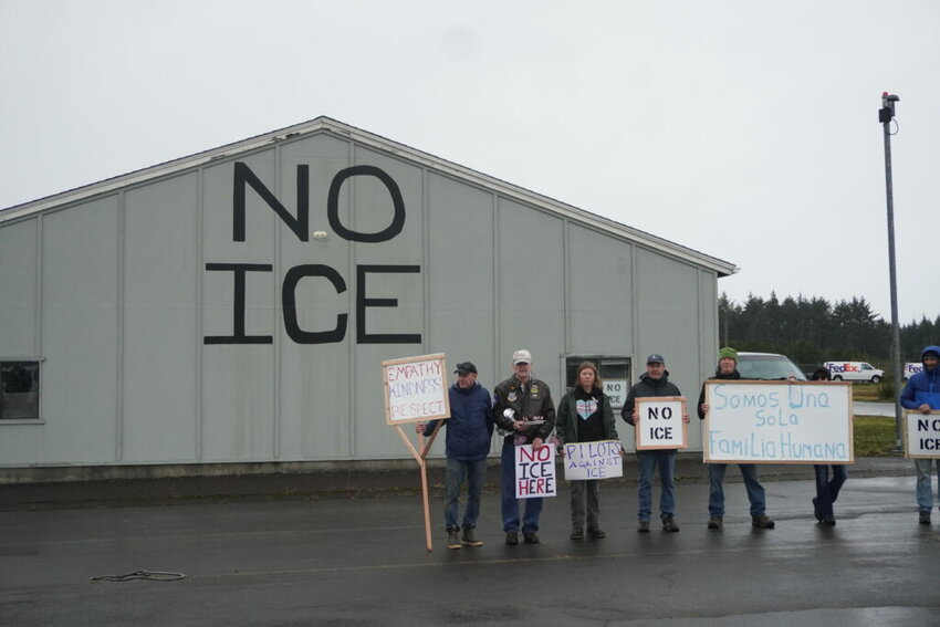 A group of local pilots and organizers stand by a hangar they have painted with &ldquo;NO ICE&rdquo;.  &ldquo;We are one human family,&rdquo; a sign in Spanish held by one demonstrator reads. (Photo by Shaanth Nanguneri/Oregon Capital Chronicle)