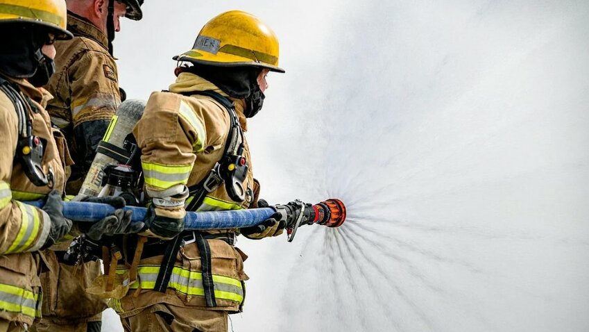 Firefighters control a high-pressure hose during a live fire training exercise.