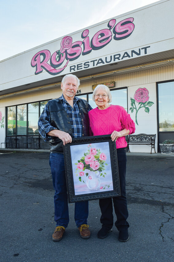 Rosie and LeRoy Woods hold a painting of pink roses by Rosie. Rosie Woods opened Rosie&rsquo;s Restaurant in 1985, and she and her husband, LeRoy Woods, have been married nearly 69 years and remain closely involved in the Woodland restaurant.