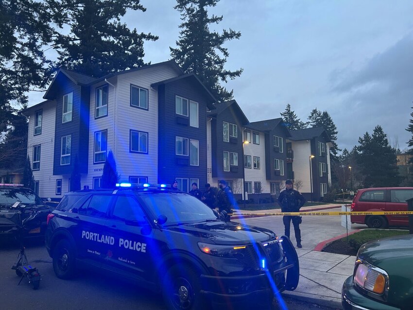 Portland police officers stand behind police tape in front of an apartment building in east Portland. (Photo by Alex Baumhardt/Oregon Capital Chronicle)