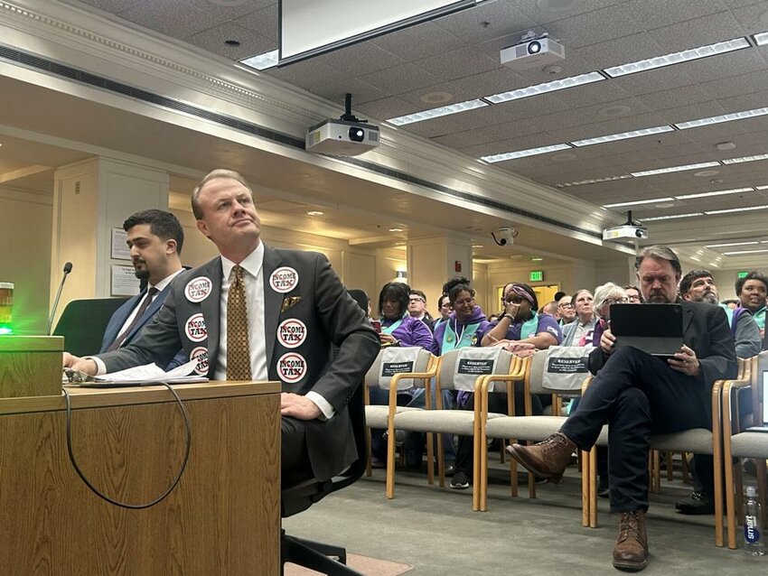Anti-tax activist Tim Eyman testifies against the income tax bill. Seated behind him in the front row of chairs is Let's Go Washington founder Brian Heywood.