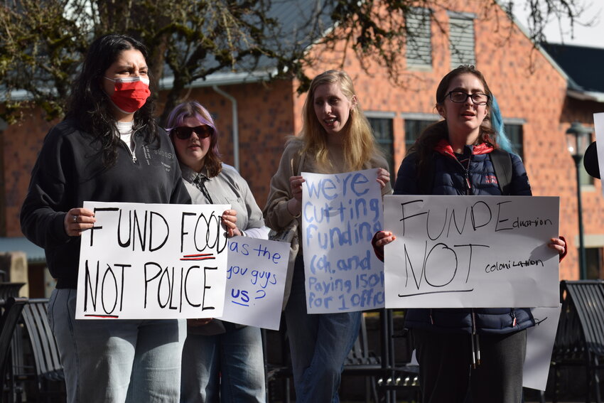 Students wave signs outside the WSU Vancouver Dengerink Administration Building on Wednesday, Feb. 4. The group protested the swearing-in of a new officer taking place inside the building at Washington State University Vancouver, citing misplaced cost priorities.