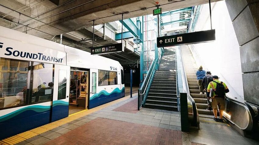 A Sound Transit Link light rail train is stopped at a station as riders use the stairs and escalator to exit.