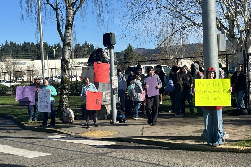 Protesters hold signs across the street from Mark Morris High School Tuesday, Feb. 10. They criticized what they described as a lack of response from the school after several students were accused of sexual assault. Two arrests were made in the case on Thursday.
