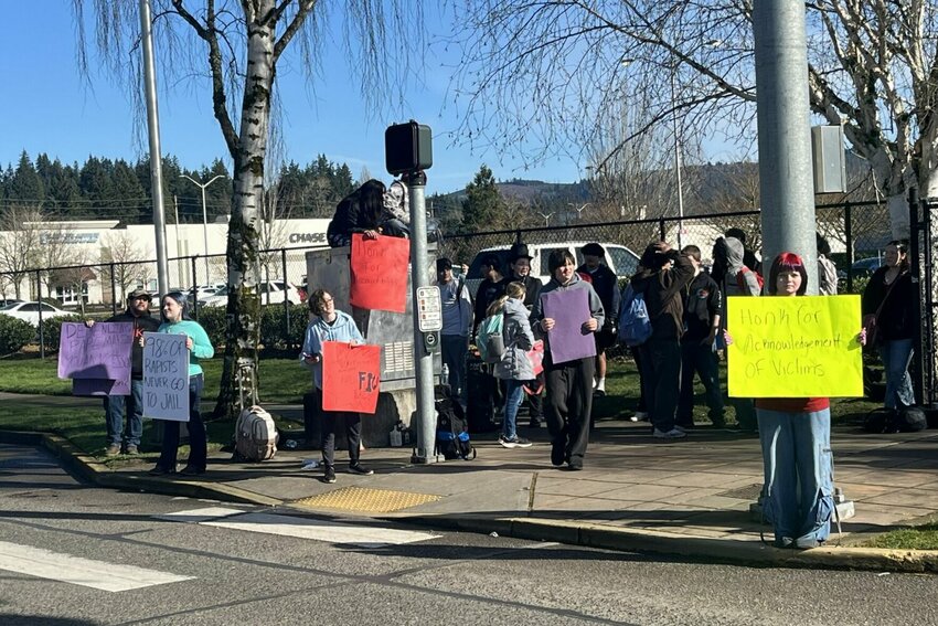 Protesters hold signs across the street from Mark Morris High School Tuesday, Feb. 10. They criticized what they described as a lack of response from the school after several students were accused of sexual assault. Two arrests were made in the case on Thursday.