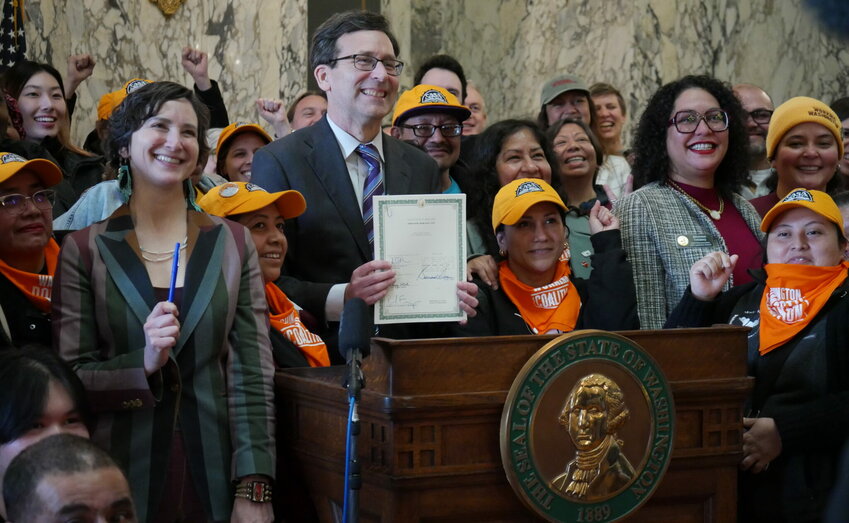 Governor Bob Ferguson appears with supporters of the bill after signing the legislation into law on March 9, 2026. House Bill 2355 establishes labor rights for nannies, gardeners and other domestic workers. (Aspen Ford/Washington State Standard)