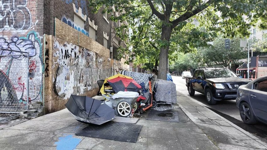 A homeless encampment with personal belongings and makeshift shelter is seen along a sidewalk in Seattle.