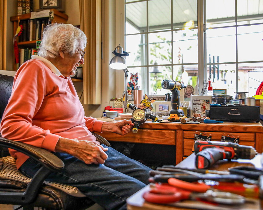 At 95-years old, local artist Gloria Lindquist examines one of her handmade art pieces at her home workshop, where she transforms recycled metal materials into whimsical creations on Wednesday, March 18.